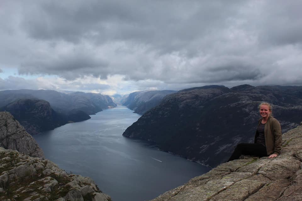 Een vrouw met blond haar zit op het randje van de Preikestolen in Noorwegen